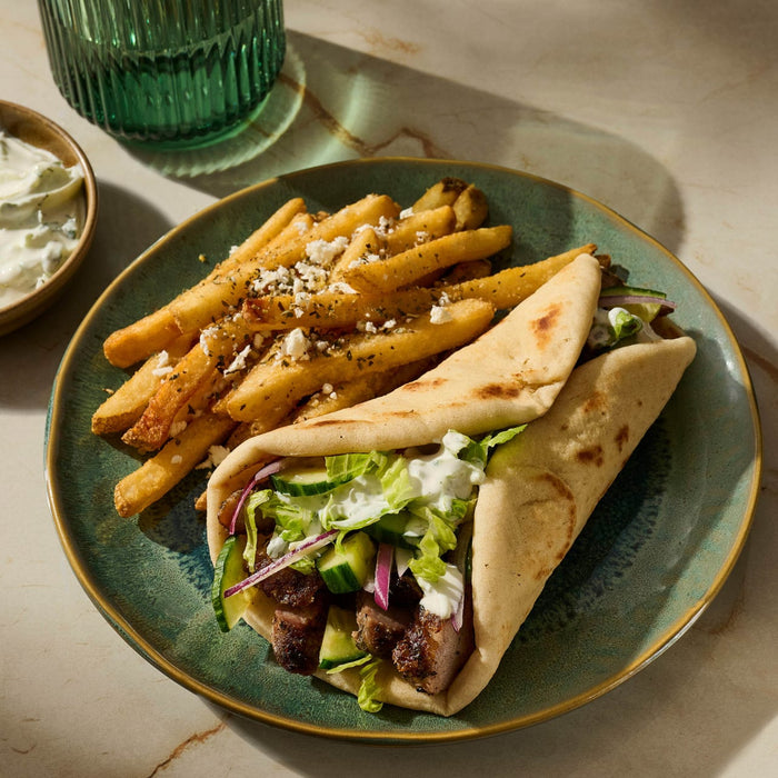 A plate with a gyro sandwich, fries topped with feta cheese, and a side of tzatziki sauce.