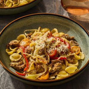 A bowl of pasta with sausage, peppers, and onions, topped with grated cheese.