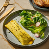 A plate with a rolled omelet topped with herbs, a side salad with radishes, and a piece of toast, showcasing a balanced and appetizing meal.
