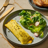 A plate with a rolled omelet topped with herbs, a side salad with radishes, and a piece of toast, showcasing a balanced and appetizing meal.