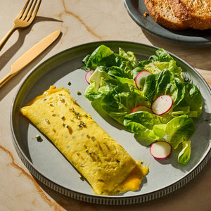A plate with a rolled omelet topped with herbs, a side salad with radishes, and a piece of toast, showcasing a balanced and appetizing meal.