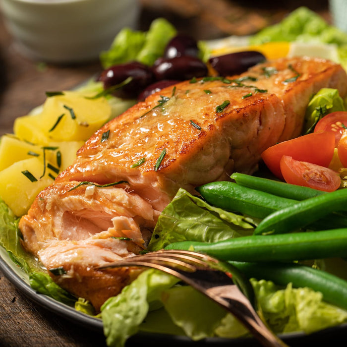 A plate of salmon with green beans, potatoes, and tomatoes.