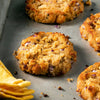 Four golden brown patties with red onion pieces on a silver baking sheet.