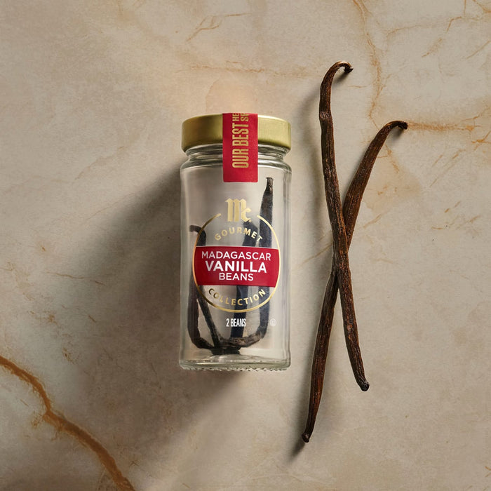 A jar of Nielsen-Massey Madagascar Vanilla Beans sits next to two loose vanilla beans.