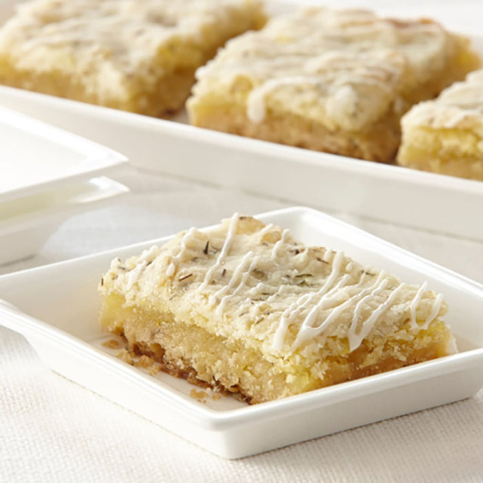 A close-up of a lemon bar with a white glaze on top, sitting on a white plate.