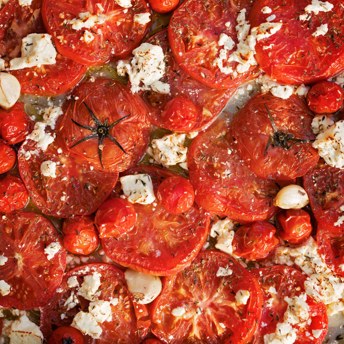 A close-up of a dish of roasted tomatoes with feta cheese and herbs.