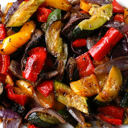 A close-up of a plate of roasted vegetables, including red peppers, yellow peppers, zucchini, and onions.