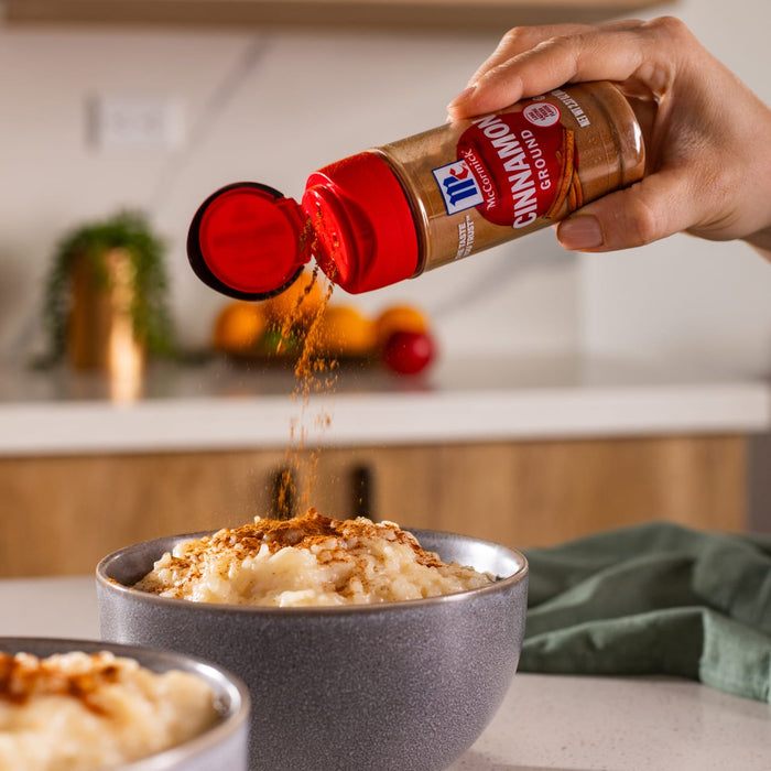 A hand sprinkles McCormick Cinnamon on a bowl of rice pudding.