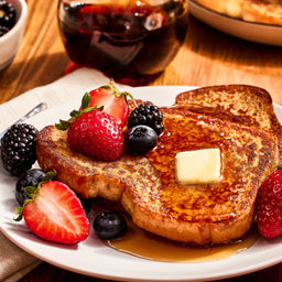 A plate of french toast with strawberries, blueberries, and blackberries, topped with butter and syrup.