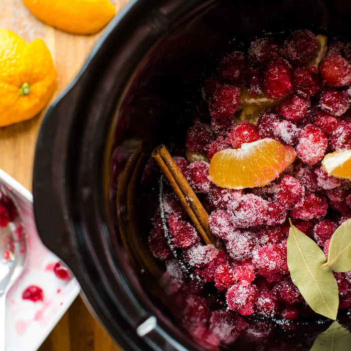 A slow cooker filled with cranberry sauce, garnished with orange slices and cinnamon sticks, suggesting a homemade holiday dish.