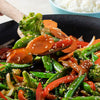 A close-up of a wok full of stir-fried vegetables with sesame seeds.