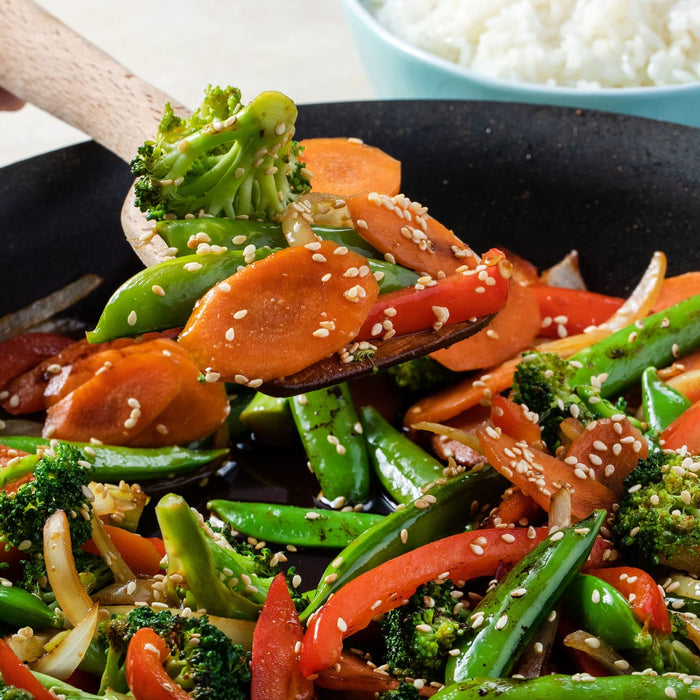 A close-up of a wok full of stir-fried vegetables with sesame seeds.