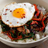 A bowl of rice topped with a fried egg, sauteed vegetables, and sesame seeds.
