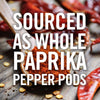 A wooden spoon filled with paprika powder, surrounded by whole red pepper pods.