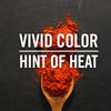A wooden spoon filled with red chili powder on a black background with the text Vivid Color Hint of Heat above it.
