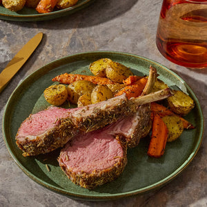A plate of roasted lamb chops with potatoes and carrots is presented on a green plate.