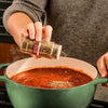 A person adds McCormick Italian Herb Seasoning to a pot of simmering tomato sauce.