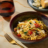 A bowl of pasta with tomatoes and cheese is presented with a glass of wine and a fork, suggesting a fine dining experience.
