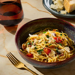 A bowl of pasta with tomatoes and cheese is presented with a glass of wine and a fork, suggesting a fine dining experience.