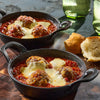Two small cast iron skillets filled with meatballs in tomato sauce topped with melted cheese, served with biscuits.