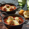 Two small cast iron skillets filled with meatballs in tomato sauce topped with melted cheese, served with biscuits.