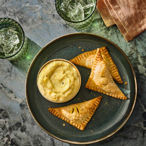 A plate with triangular pastries and a bowl of dipping sauce, suggesting a delicious appetizer or snack.