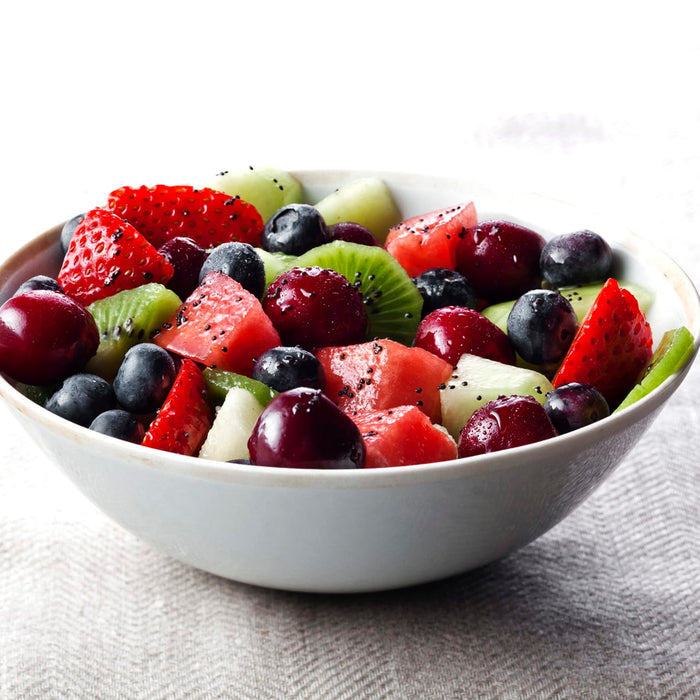 A white bowl filled with a fruit salad of watermelon, kiwi, strawberries, blueberries, and cherries.