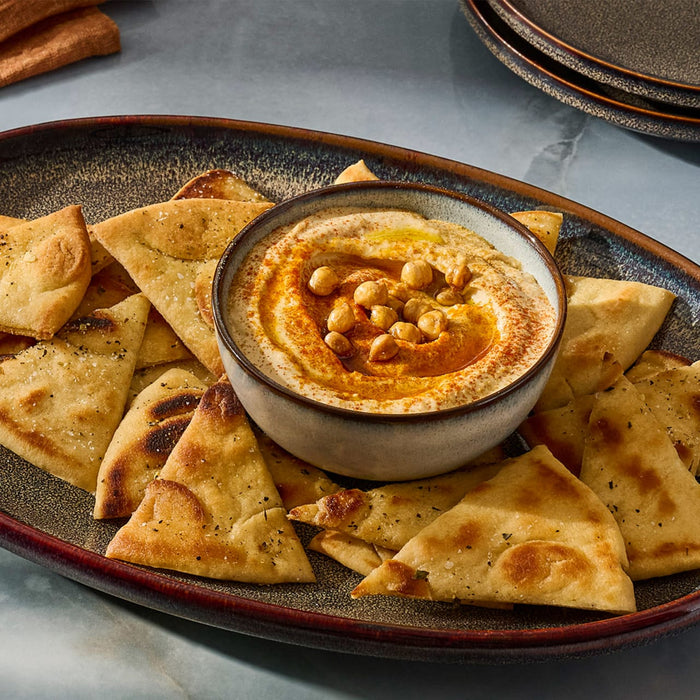 A bowl of hummus surrounded by pita bread triangles is presented on a platter, showcasing a delicious and inviting appetizer.