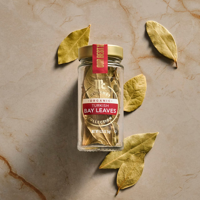 A jar of Trader Joe's bay leaves is surrounded by loose bay leaves on a marble surface.