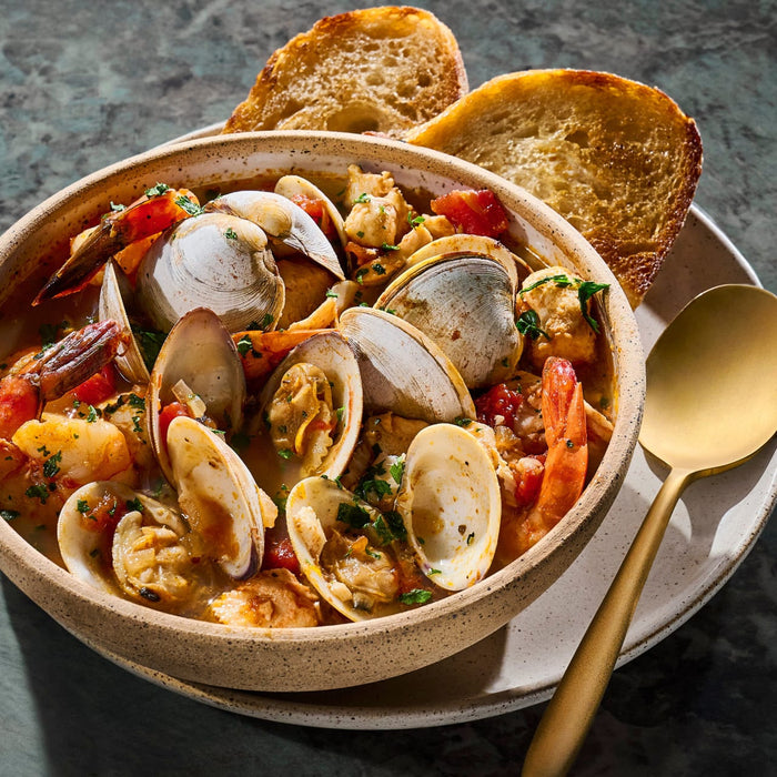 A bowl of seafood stew with clams, tomatoes, and toasted bread, showcasing a hearty and flavorful meal.