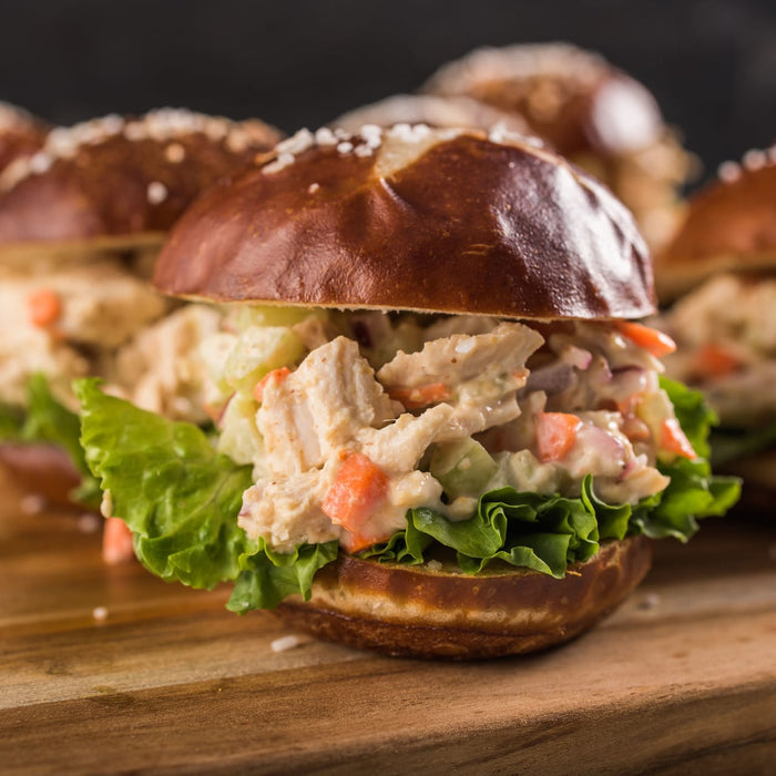 A close-up of a pretzel roll filled with chicken salad and lettuce.