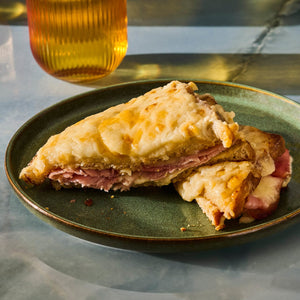 A Croque Monsieur sandwich, cut in half and served on a green plate, with a beverage in the background.