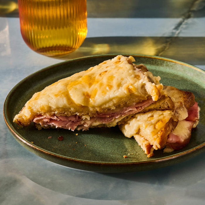 A Croque Monsieur sandwich, cut in half and served on a green plate, with a beverage in the background.