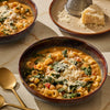 A bowl of creamy pasta soup with spinach and grated Parmesan cheese is presented in a warm, inviting setting.