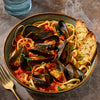 A bowl of linguine pasta with mussels in a rich red tomato sauce, subtly spiced with Mccormick Gourmet Red Pepper Crushed Organic, and served with toasted bread.