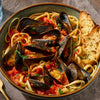 A bowl of linguine with mussels in a tomato-based sauce, served with garlic bread.