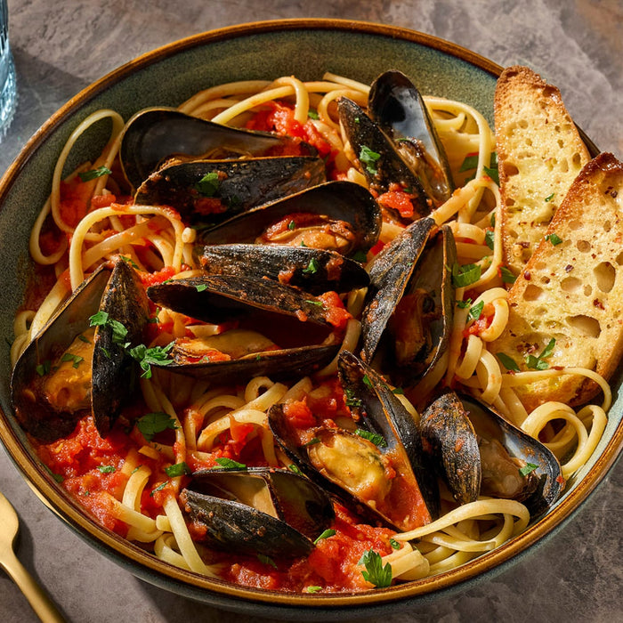 A bowl of linguine with mussels in a tomato-based sauce, served with garlic bread.