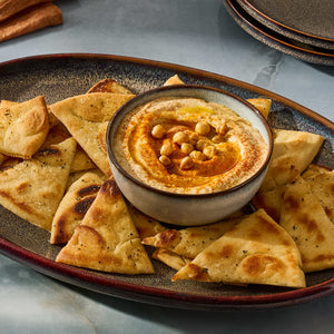 A platter of pita bread triangles surrounds a bowl of hummus topped with chickpeas and paprika.