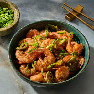 A bowl of crispy fried shrimp garnished with sliced green peppers, ready to eat with chopsticks.