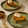 Two slices of pumpkin pie with whipped cream on green plates, showcasing a delicious dessert.