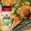 A container of McCormick Garlic Powder next to a dish of roasted chicken potatoes carrots and greens.