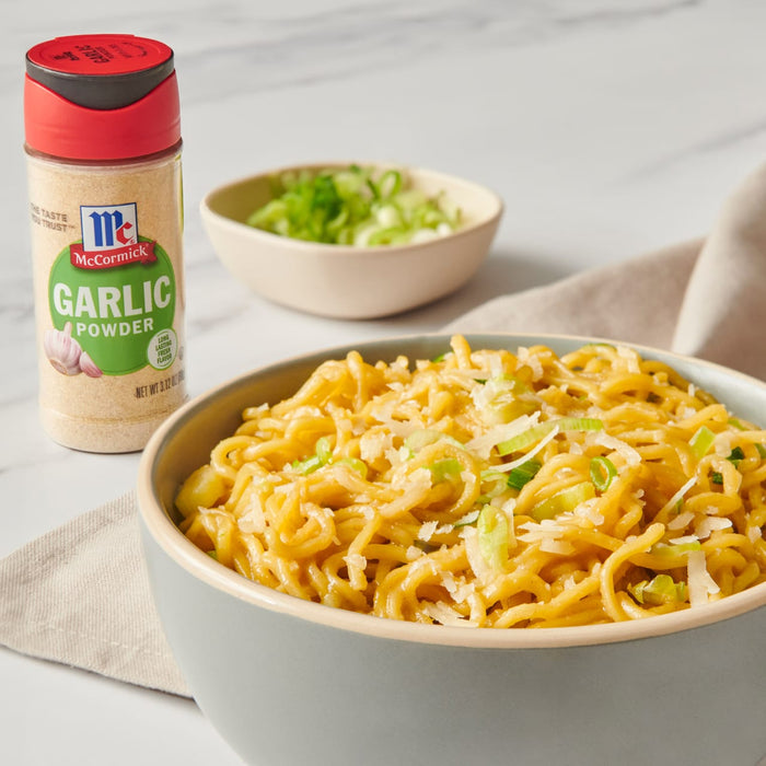 A bowl of noodles with green onions and parmesan cheese, next to a McCormick Garlic Powder container.
