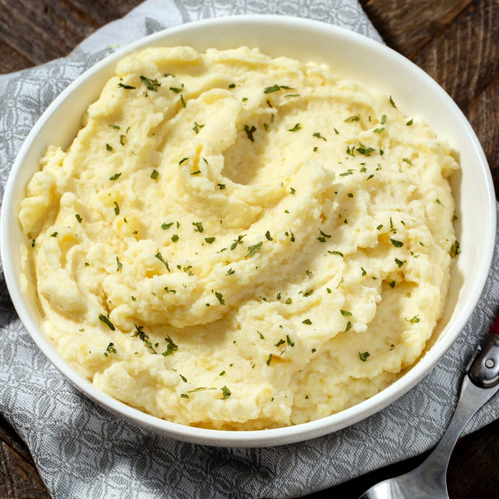 A bowl of mashed potatoes with parsley on top.