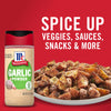 A container of McCormick Garlic Powder next to a plate of seasoned potatoes.
