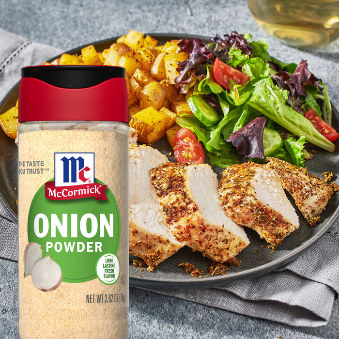 A bottle of McCormick Onion Powder next to a plate of grilled chicken with a side of greens and a lemon wedge.