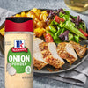 A container of McCormick Onion Powder next to a plate of seasoned chicken, potatoes, and salad.