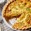 A quiche with a flaky crust and a creamy egg filling topped with green onions and spices.