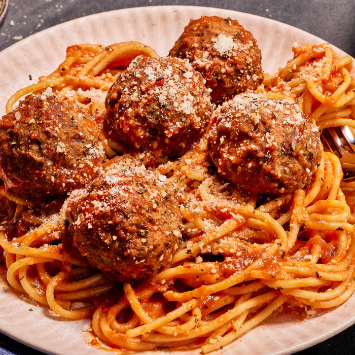 Spaghetti with meatballs and tomato sauce topped with parmesan cheese.