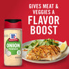 A bottle of McCormick Onion Powder next to a plate of grilled chicken with a side of greens and a lemon wedge.