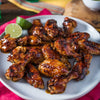 A plate of glazed chicken wings with lime wedges.
